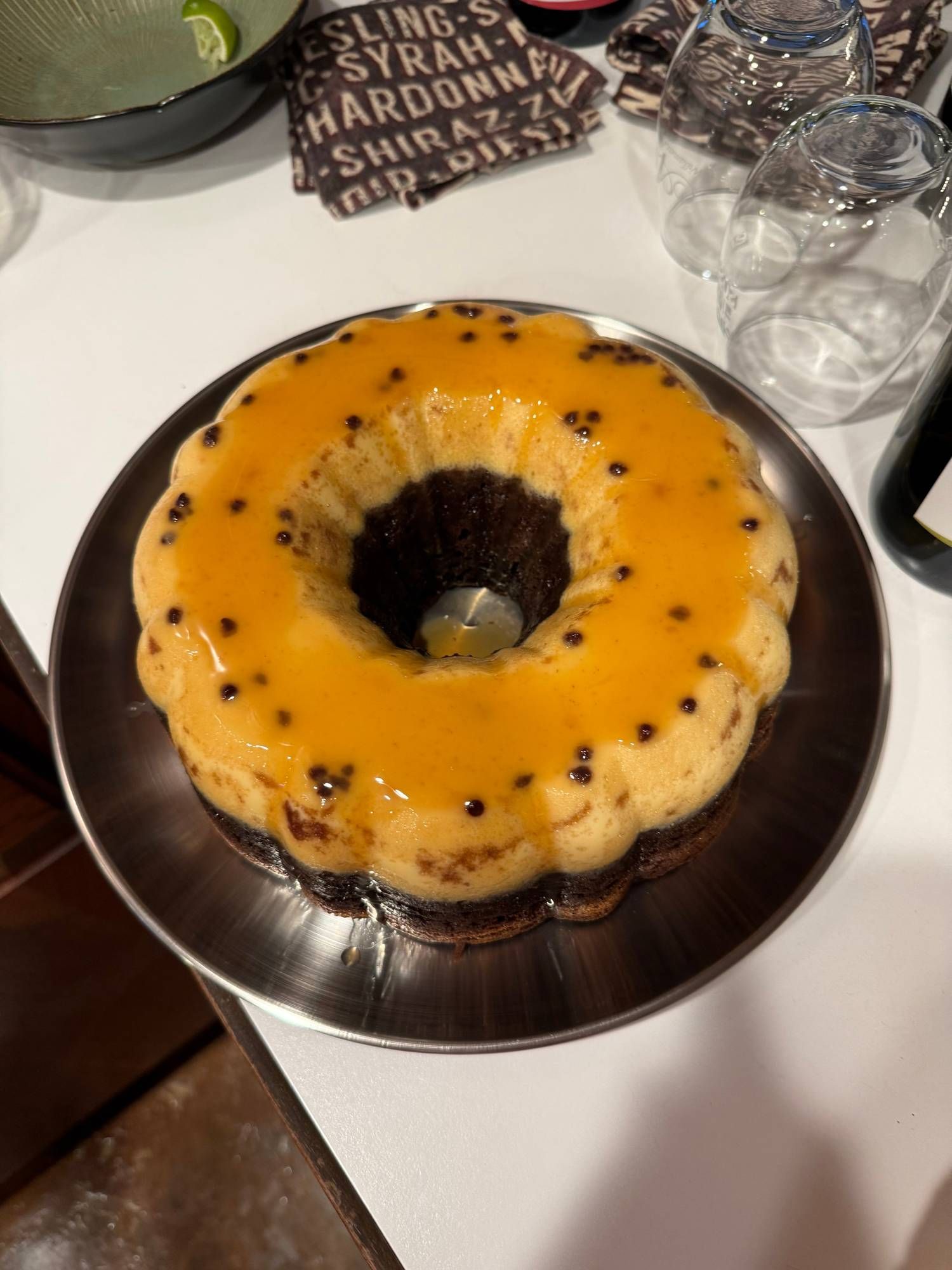 A chocoflan — a ring-shaped dark chocolate cake topped with a golden flan layer and caramel — on a metal plate.